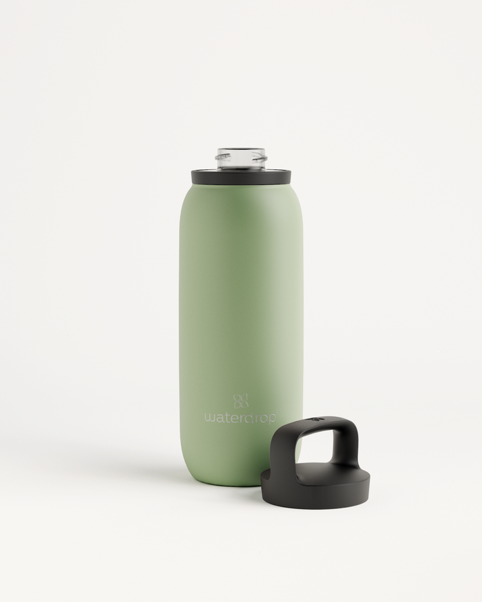 All-Purpose Thermo · Dop met drinktuit, een matte sage-groene geïsoleerde waterfles van waterdrop®, staat rechtop met een zwart schroefdop voorzien van draaghendel ernaast, ideaal voor koude dranken.