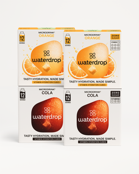 Vier kartonnen dozen met waterdrop® Microdrink Cola Orange Set 3+1. Twee dozen Cola en twee Orange, elk met 12 porties, vitaminen (C, B1, B2, B3, B5, B6, B12), zonder suiker.