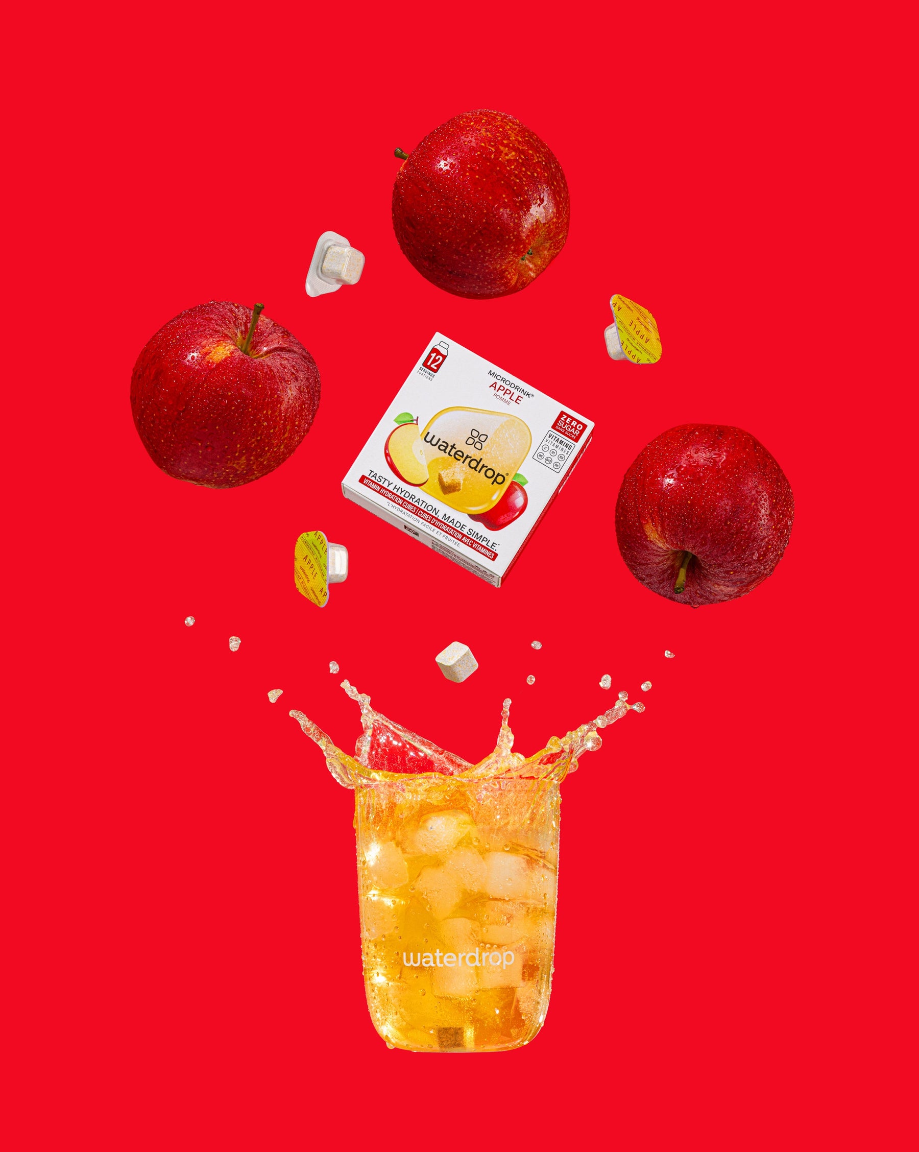 Set: 5 jaar waterdrop in Nederland 4+1, toont drijvende rode appels, een doos waterdrop® Microdrink Apple, en enkele microdrink pods en smaakblokjes naast een glas van fris appelkleurig ijsdrankje.