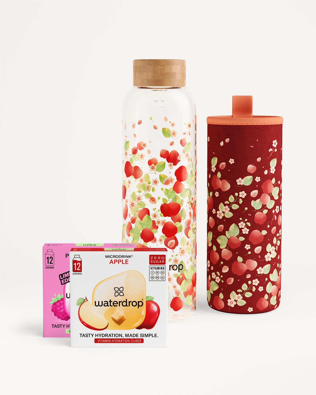 APPEL Set met fles: doos microdrink® APPLE hydratieblokjes zonder suiker, met een glazen fles met appelbloesemmotief en bijpassende neopreen hoes. Raspberry-pink doos zichtbaar achter de appeldoos.