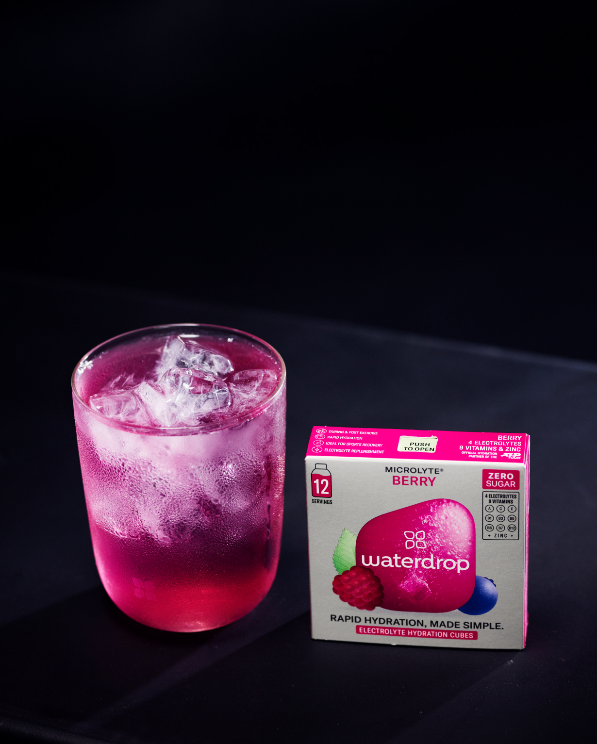 Dunlop ATP Tour Set: Tennisballen + Fles + Microlyte; een roze-paars drankje in een tuitglas met condens naast waterdrop “Microlyte Berry” doos, een 12-pack elektrolytenmix zonder suiker.