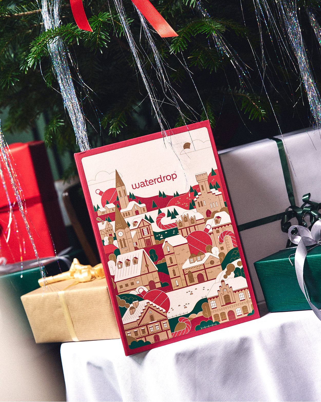 Cadeauset met glazen fles APPEL, verpakt in een feestelijke adventskalender van waterdrop®, uitgestald onder een versierde kerstboom, omringd door cadeaupapier en slingers. Perfect voor een magische, fruitige kerstbeleving.