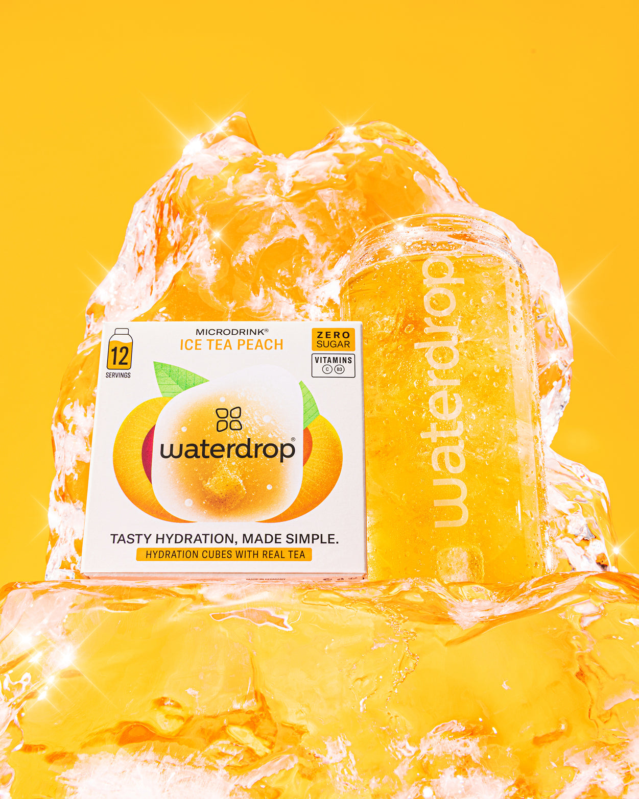 Starterset Glass Deluxe: Waterdrop's Microdrink Ice Tea Peach in een fel productshot. De doos met 12 suikervrije porties en vitaminen staat naast een glas sprankelende perzik-ijsthee op ijsblokken.