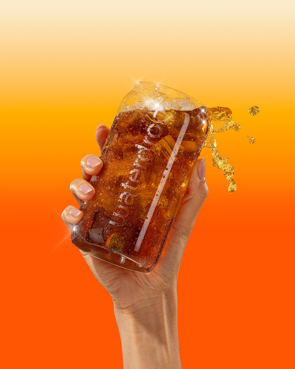 Hand houdt stevig een COLA Glass Can van helder borosilicaatglas vol donkere frisdrank met ijs en citrusschijf, liquid splash bovenop. Limited Edition, perfect voor duurzame, verfrissende drankervaring.