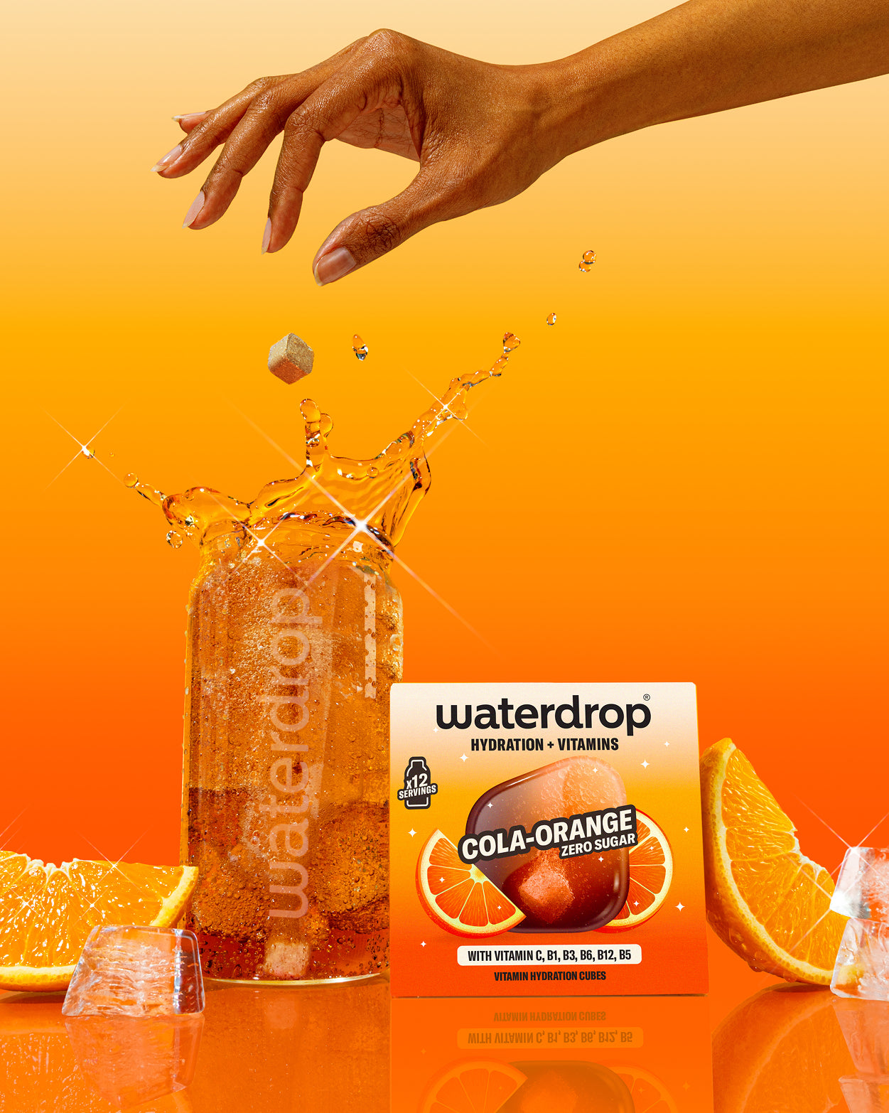 Frisdrankenset: Een Waterdrop-glas bruisend met een net gedropte Cola-Orange hydratatiecube, vergezeld van verse sinaasappelpartjes en ijs, naast de Waterdrop-verpakking met vitamineverrijkte, suikervrije Microdrink.