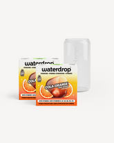 Twee dozen waterdrop COLA ORANGE vitaminehydratatieblokjes met twaalf porties elk, gepositioneerd voor een helder, cilindrisch drinkglas uit de COLA glazen blikjesset, ideaal voor duurzame consumptie.