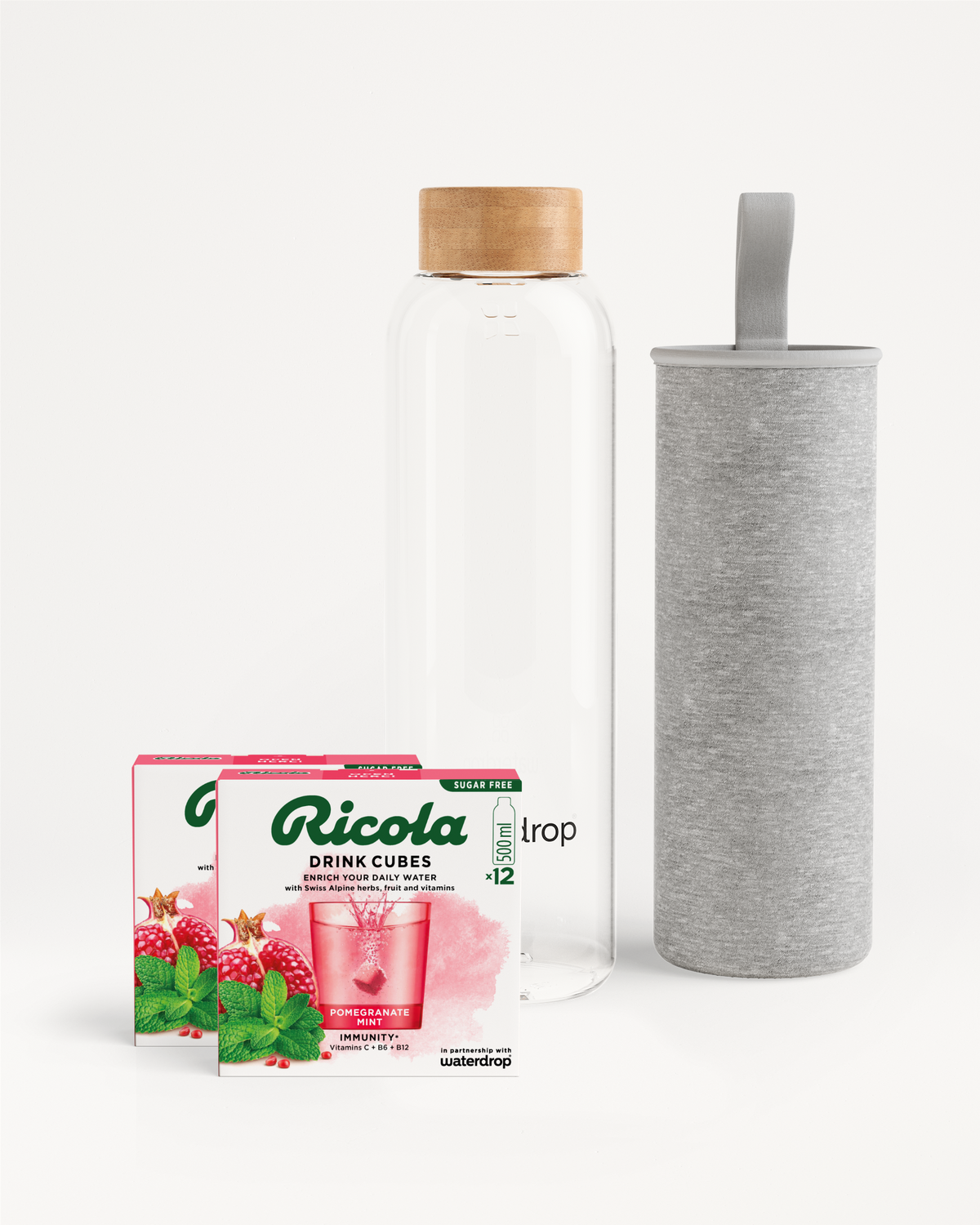 Flessenset van Ricola met twee doosjes Pomegranate-Mint Drink Cubes en een waterdrop® glazen waterfles met bamboedop, vergezeld van een grijze stoffen hoes. Ideaal voor smaakvolle hydratatie.