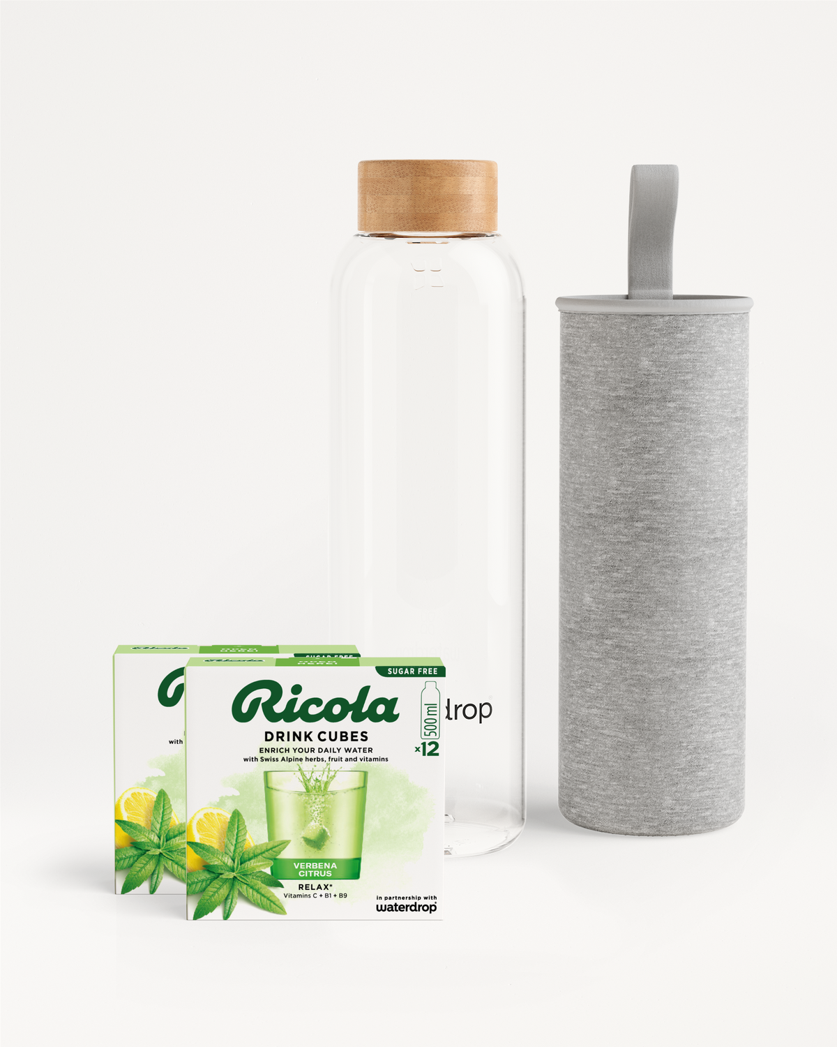 Flessenset van Ricola: een heldere waterfles van 500 ml met bamboe dop en grijze hoes, vergezeld van twee dozen Ricola Drink Cubes in Verbena Citrus-smaak voor een verfrissende hydratatie-ervaring.