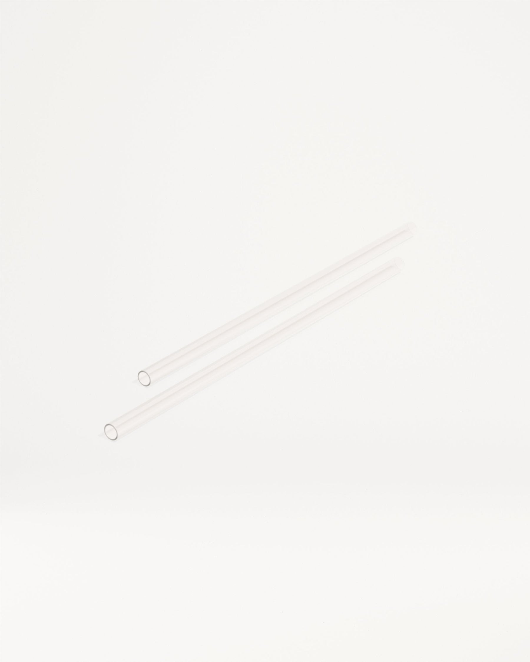 Twee lange, slanke, transparante buisjes, vergelijkbaar met glazen of plastic rietjes, liggen diagonaal. Dit zijn de Explorer Thermo Tumbler Straws, perfect voor waterdrop®'s innovatieve drinkproducten.