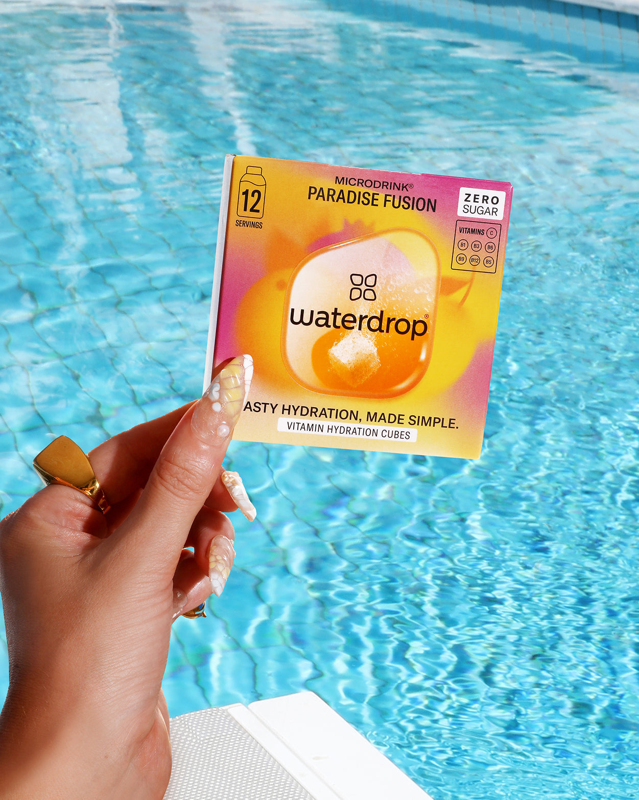 PARADISE FUSION: Een hand houdt een kaart met een label van een verfrissende mix van sinaasappel en mango voor een zwembad, perfect voor een zomerse ervaring waar je ook bent.