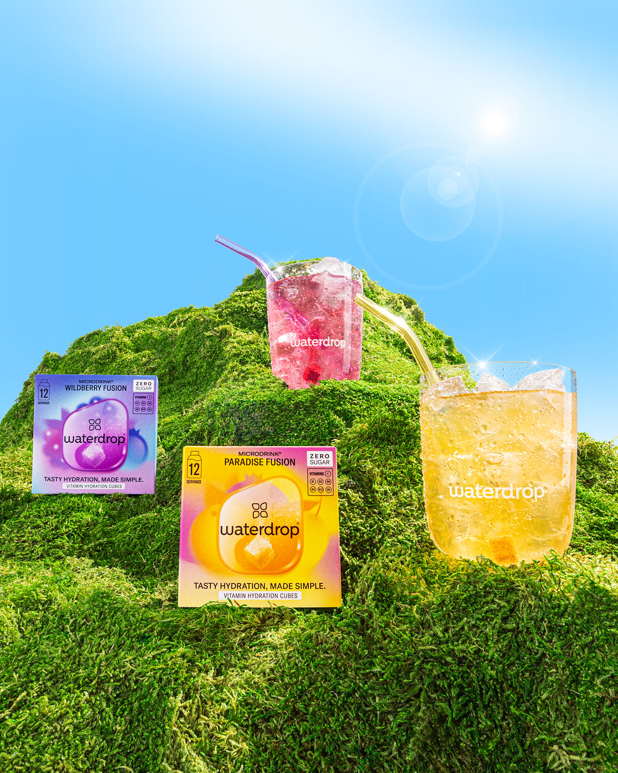 Zomer Bestseller Set: Een glas roze drank met een rietje, omringd door andere verfrissende drankjes op een groene heuvel, belichaamt de zomerse smaken van sinaasappel, grapefruit, Paradise en Wildberry Fusion.