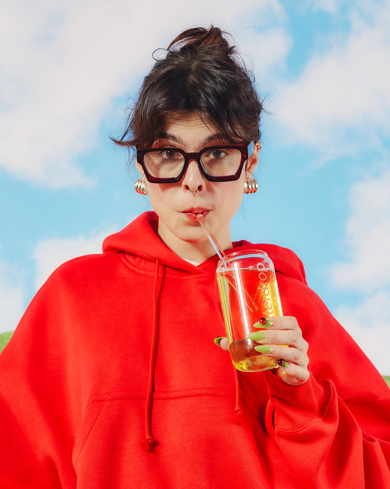Een jong persoon drinkt uit een doorzichtig, frisdrankvormig glas met een gele drank, onderdeel van de Apple Sparkle Set van waterdrop® NL, compleet met een herbruikbaar glazen rietje.