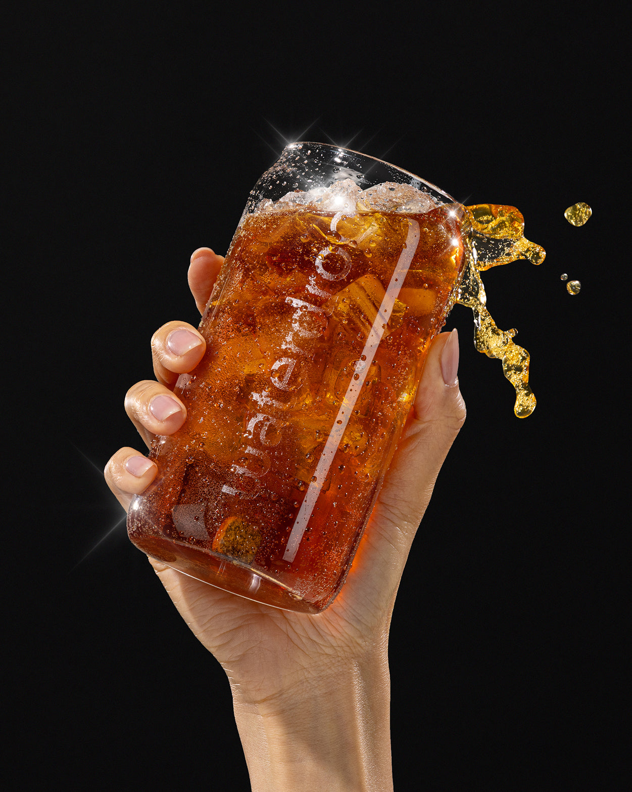 Hand houdt een glazen tumbler vast met ijs en bruisende donkere COLA ORANGE Set 3+1, met zichtbare bubbels en een kleine splash. Geen suiker, vol smaak, essentiële vitamines.