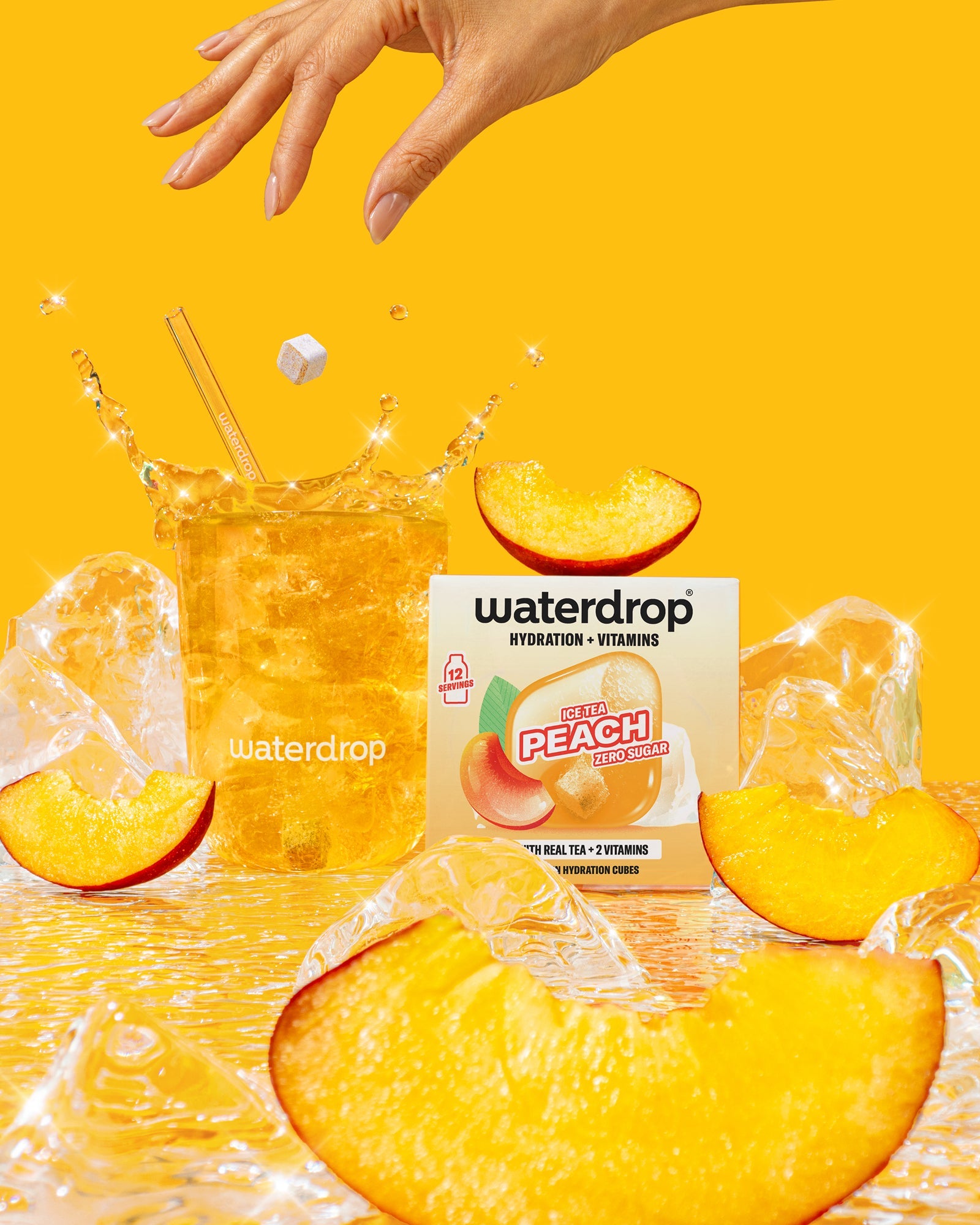 Set voor warme zomerdagen: Een glas met ijsthee perzik van Waterdrop, met ijsklontjes, een zwevende hydratatiecube, roerstokje, perzikpartjes, en de doos met Hydration + Vitamins – Ice Tea Peach – Zero Sugar.