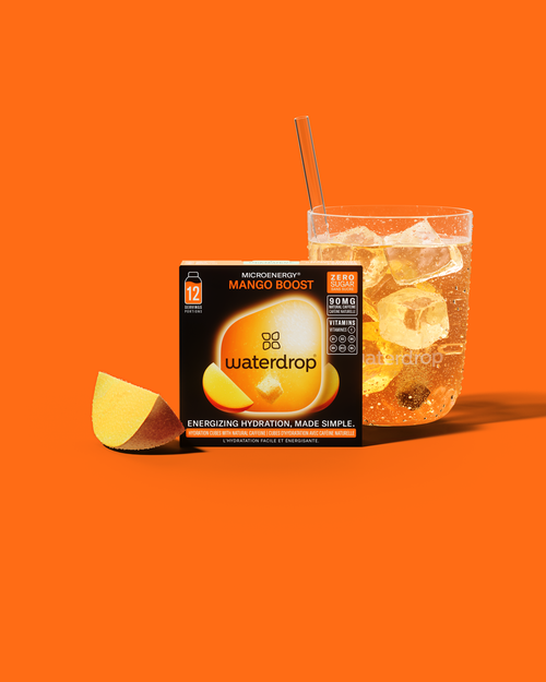 Close-up van een MANGO BOOST tube naast een drankje; een krachtige combinatie van mango en guayusa voor een suikervrije energieboost. Perfect voor diegenen die behoefte hebben aan een opkikker onderweg.