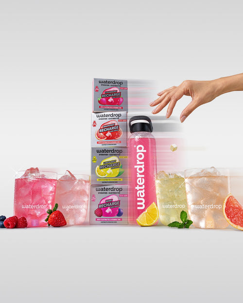 Microlyte RECHARGE Set 3+1 met vier Waterdrop-dozen (Aardbei, Grapefruit, Citroen-Mint, Berry) en een roze Waterdrop-fles, omringd door ice-glazen met fruit en kruiden, benadrukt hydratatie en elektrolyten.