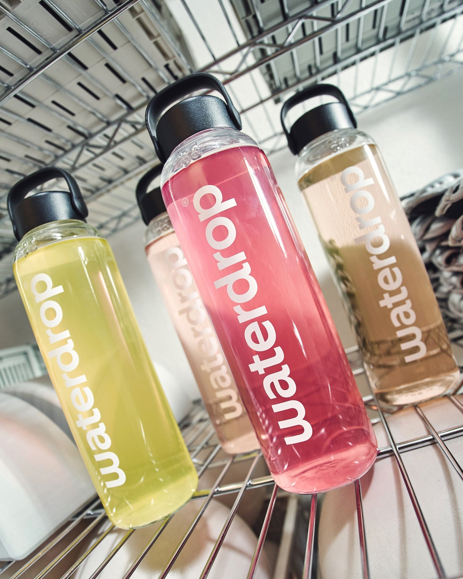 Microlyte RECHARGE Set 3+1 op een klein rek met vier doorzichtige plastic flessen, gevuld met pastelgetinte vloeistoffen: BERRY, LEMON-MINT, STRAWBERRY en GRAPEFRUIT, allemaal verrijkt met elektrolyten en vitaminen.