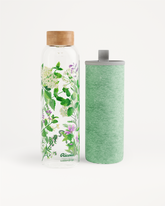 Ricola Edition Glass: Een hoge glazen waterfles met houten dop, bedrukt met kruidenillustraties, naast een bijpassende groen stoffen hoes met draaglus, speciaal ontworpen voor frisse hydratatie in samenwerking met waterdrop®.