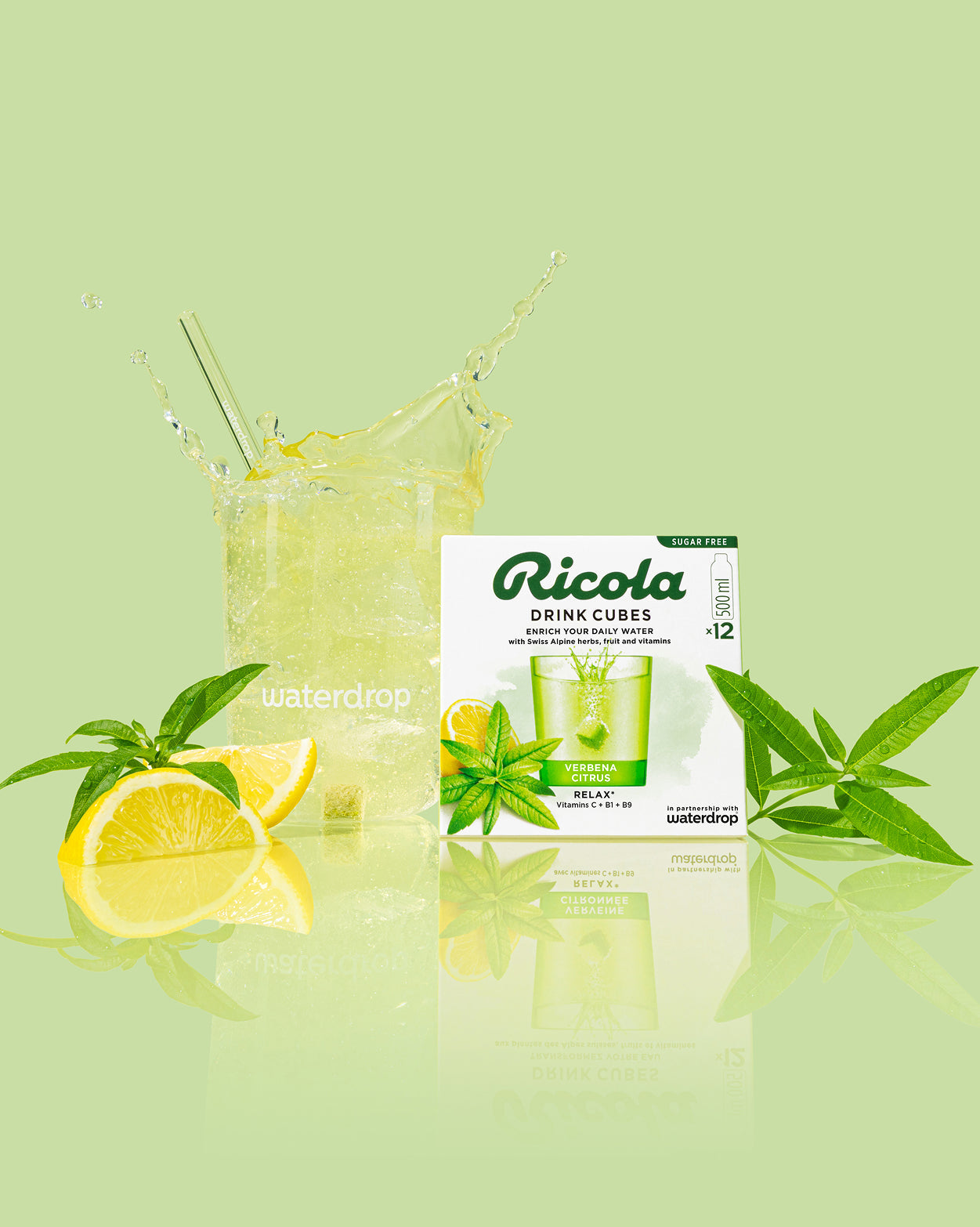 Ricola Discovery Set met Verbena Citrus Drink Cubes, toont een witte doos met 12 suikervrije blokjes, een bruisend glas met een oplosblokje en citroenpartjes, omringd door verse verbenablaadjes.