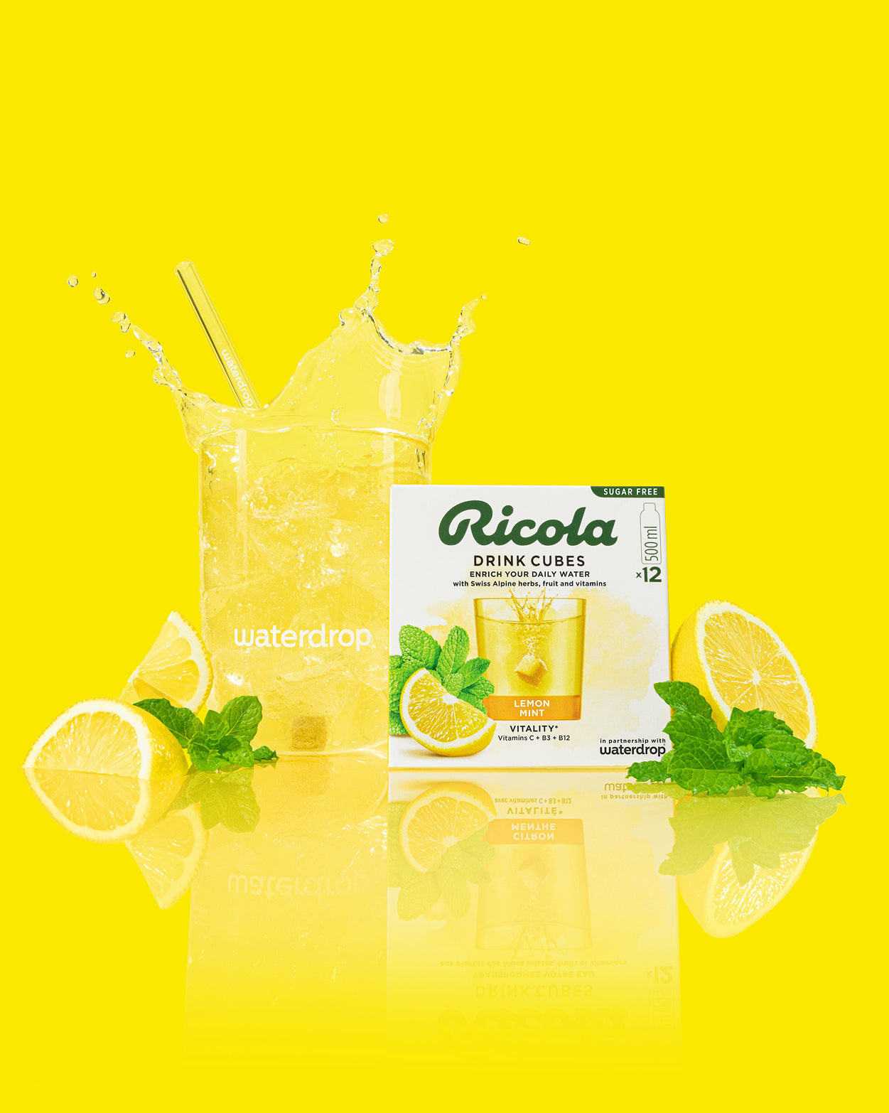 Ricola Discovery Set: Een helder glas bruiswater met waterdrop®-rietje en een doos Ricola Drink Cubes Lemon Mint Vitality. Versieringen van citroenschijfjes en munt benadrukken de verfrissende smaakbeleving.