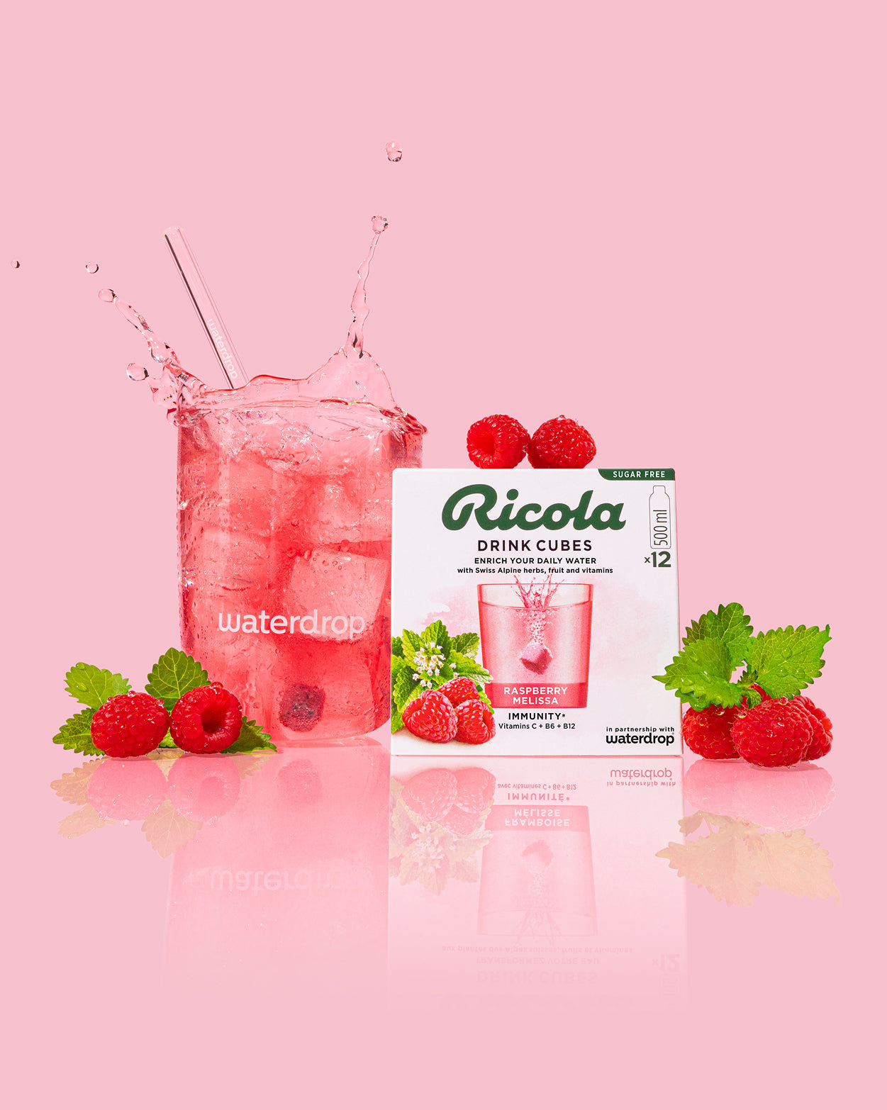 Ricola Discovery Set met waterdrop® glas gevuld met ijswater, drijvende frambozen en melissa, naast een doos Ricola DRINK CUBES framboos-melissa smaak, suiker- en calorievrij, met vitamines. Ideaal voor verfrissende hydratatie.