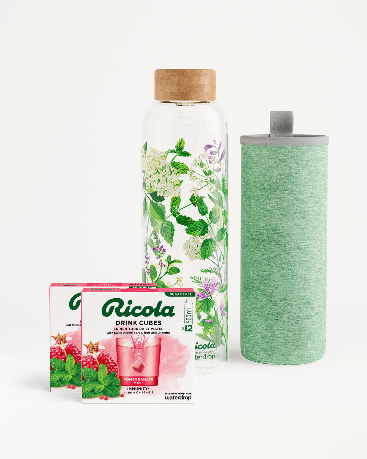 Flessenset van Ricola: Twee dozen Ricola Drink Cubes Pomegranate Mint en een limited edition glazen waterfles met houten dop en bladerprint, inclusief heather-groene isolerende hoes voor grip en bescherming.