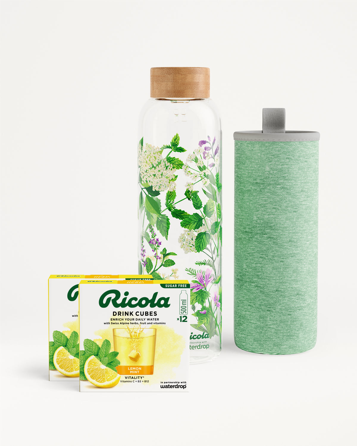 Flessenset van Ricola: Twee doosjes Ricola Drink Cubes (Lemon Mint) naast een glazen waterfles met houten dop en groene bladsierkunst, met bijpassende groene hoes. Perfect voor suiker- en caloriearm hydrateren.