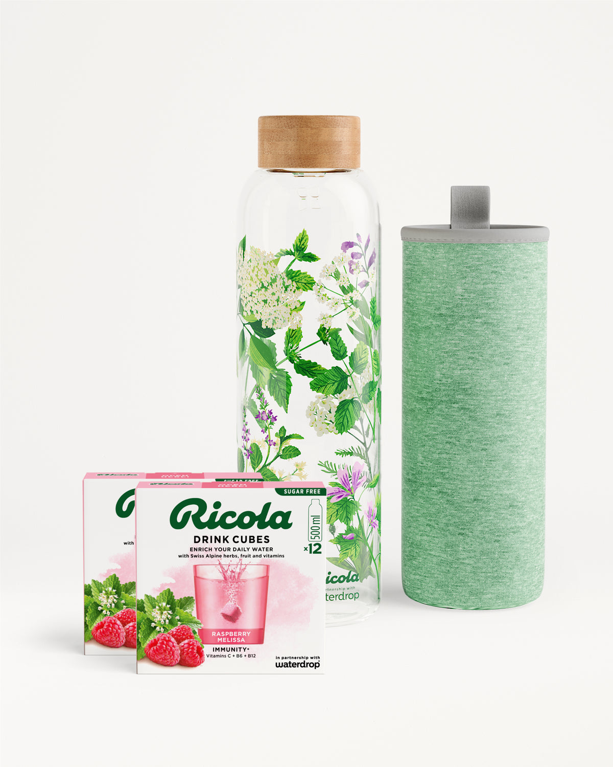 Flessenset van Ricola: Een glazen waterfles met bamboedop, groene sleeve en delicate Alpenkruidenprint, vergezeld van twee dozen Ricola Drink Cubes (Raspberry & Melissa, suikervrij) voor smaakvolle hydratatie.