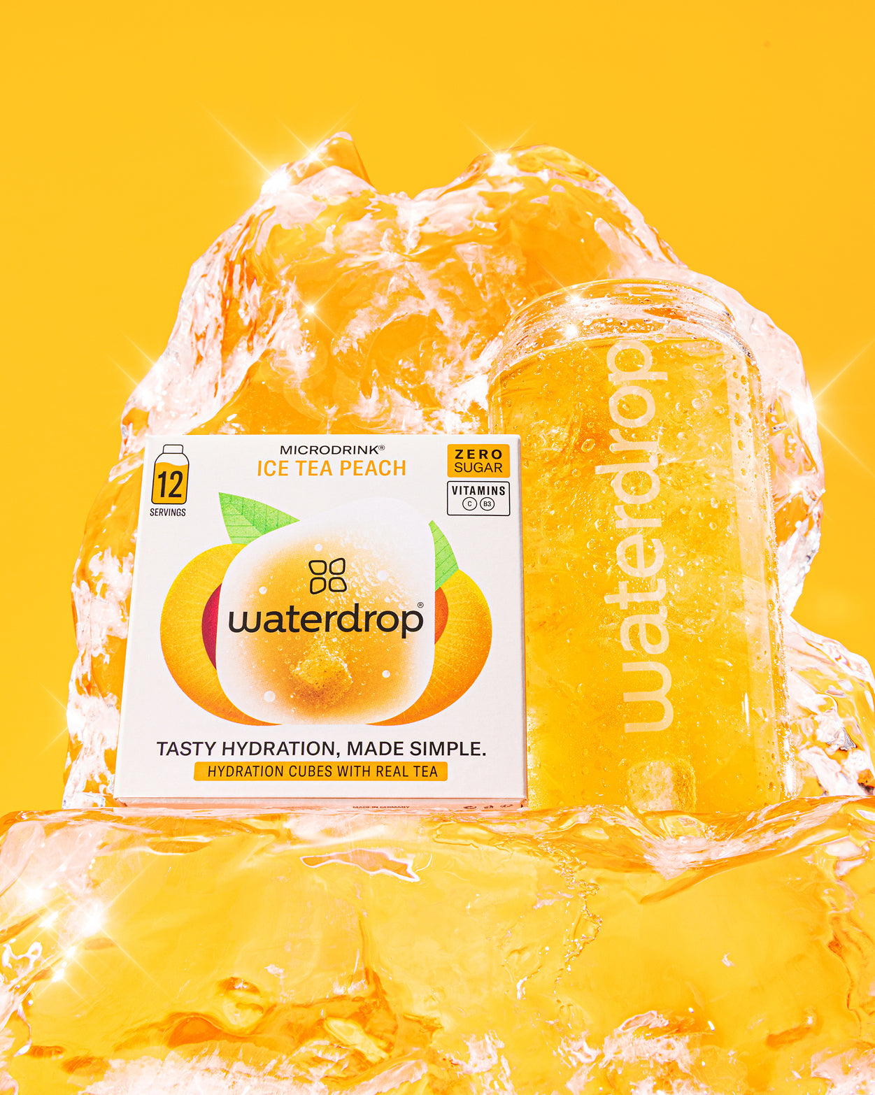 Social Mode Set met waterdrop Microdrink Ice Tea Peach: een witte doos met perzikafbeelding en een gevulde waterdrop-fles, omringd door sprankelend ijs, tegen een effen achtergrond.