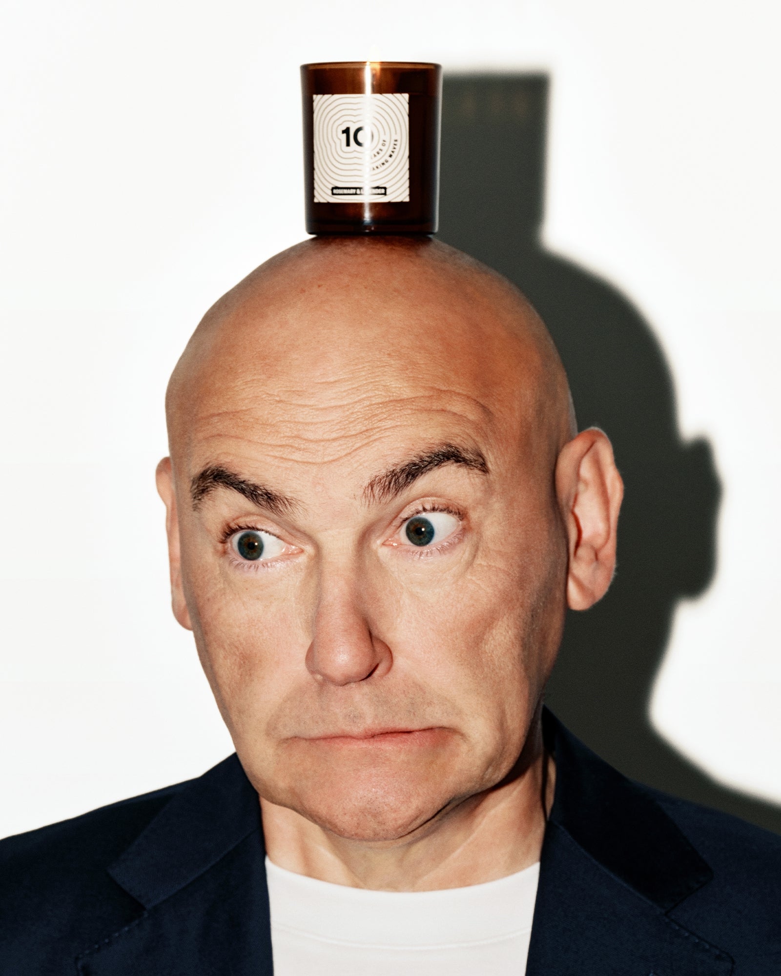 Kaal hoofd man in donker colbert, met een kleine koperen fles op het hoofd gebalanceerd.