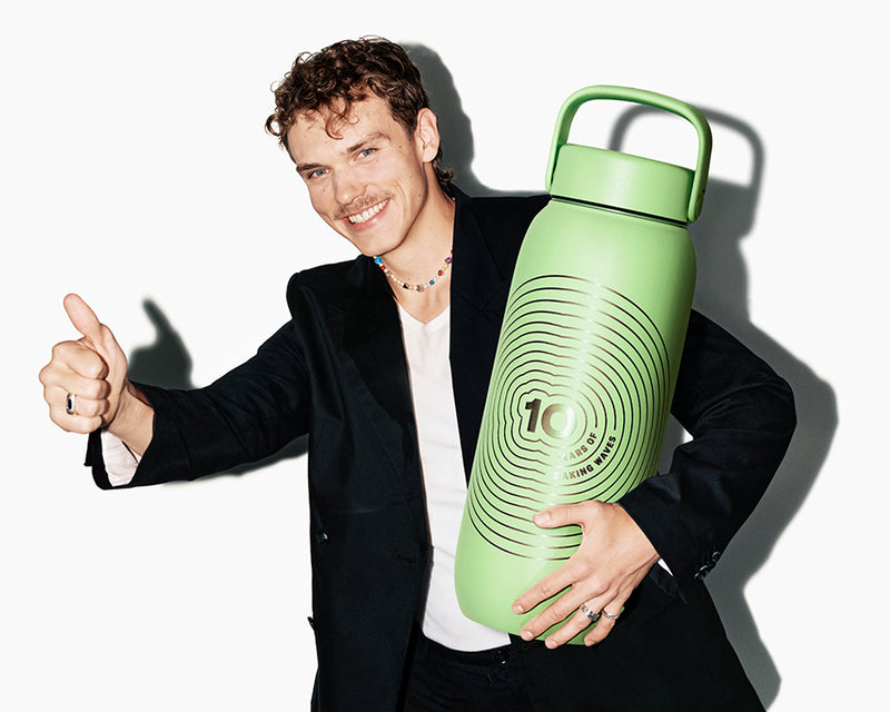 Lachende man in een blazer houdt een grote groene herbruikbare fles met handvat en geeft een duim omhoog.