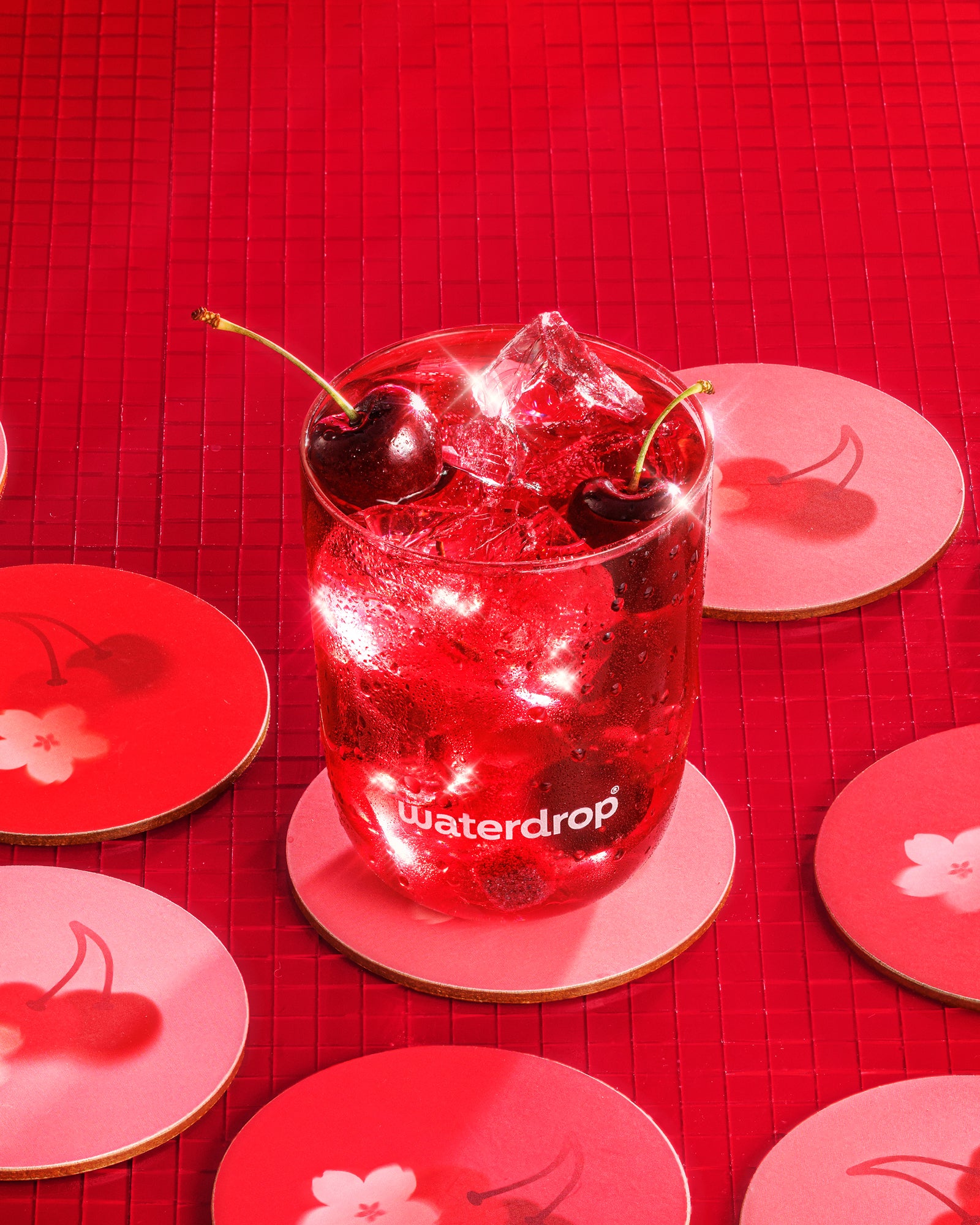 Koud rood drankje met ijs en twee kersen in een glas op een rode achtergrond met schotels met kersenmotief.
