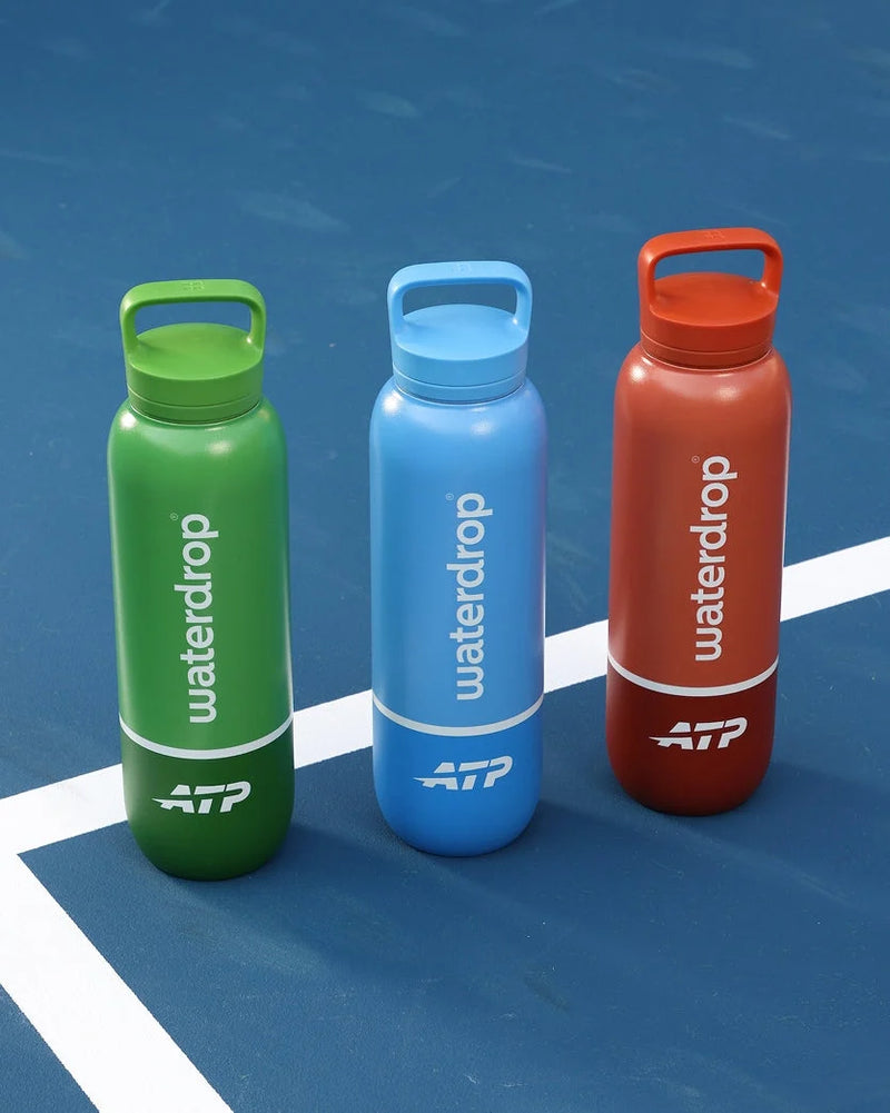 Drie sportwaterflessen op een blauw tennisveld.