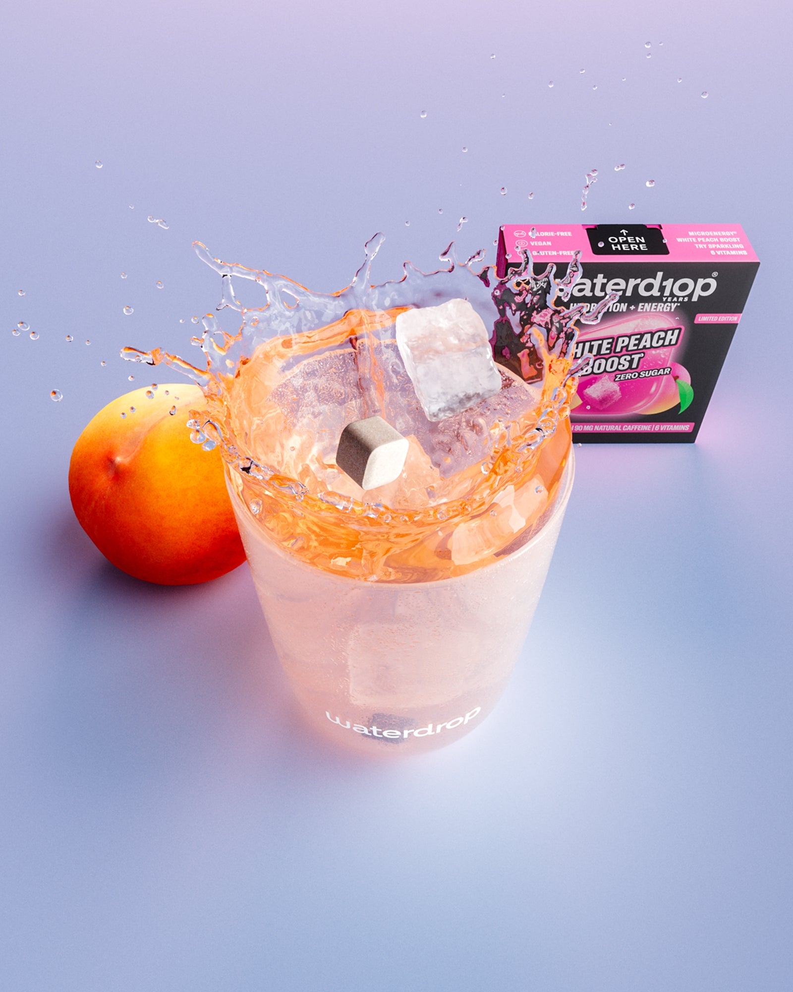 Glas met perziksm smaak en ijsblokjes, een perzik en een doos op de achtergrond.