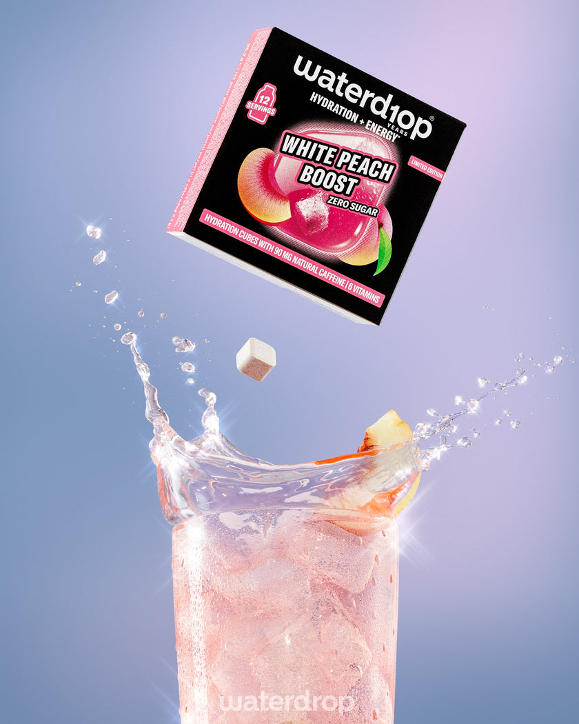 Een doos valt richting een hoog glas roze perzikdrank met stukjes perzik, terwijl het spat.