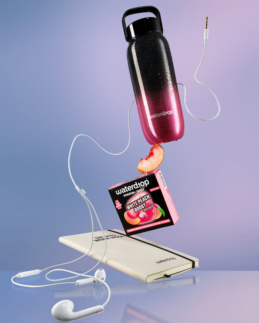 Vliegende weergave van een waterfles met zwart-proef roze verloop boven een witte powerbank, verbonden door witte kabels met een perzikpartje in de buurt.