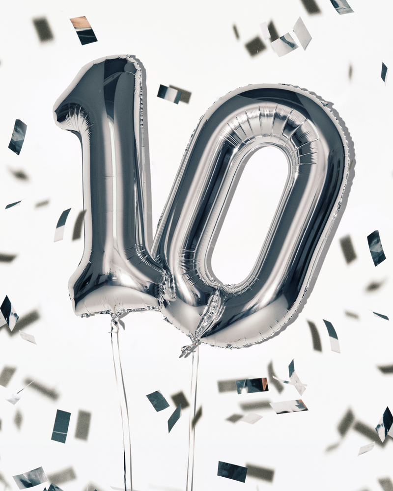 Zilveren folieballonnen in de vorm van het getal 100 met lintjes, omgeven door confetti.