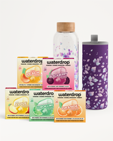 Assortiment van drankensmaken sachets in kleurrijke doosjes, plus een glazen fles met kurk en een paarse bloemmotief drinkkan.