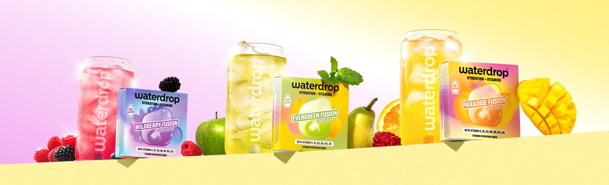 Verschillende Waterdrop-smaakversterkers in roze, paars, groen en geel flessen op een gele plank met fruit.