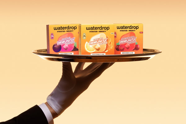 Gesteunde hand met handschoen houdt een dienblad met drie kleine doosjes tegen een oranje achtergrond.