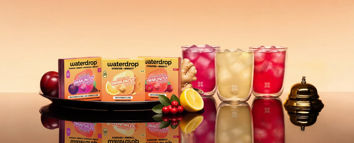 Dienblad met sapjes in dozen en drie kleurrijke fruitige dranken in hoge glazen op een reflecterende ondergrond.