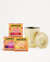 Drie vitamine-drankmixdozen en een beige mok met deksel op een witte achtergrond.