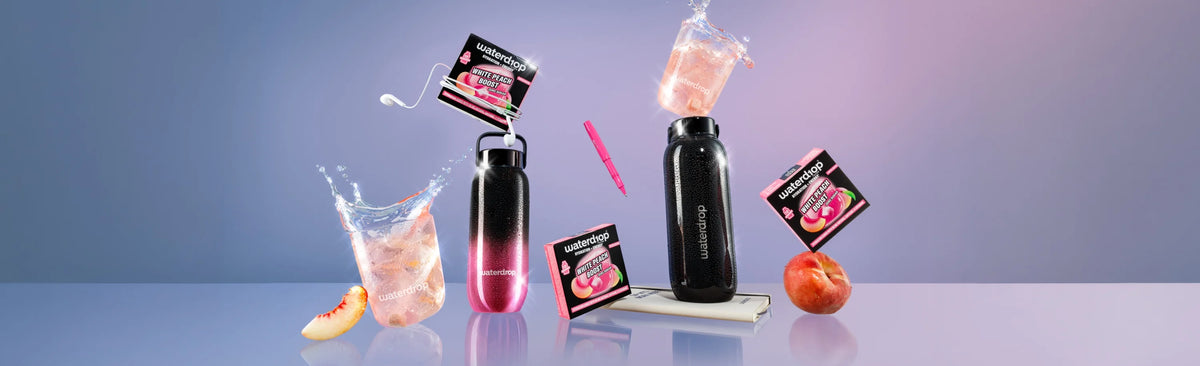 Verzameling zwarte flessen met roze vloeistof en kleine productverpakkingen verspreid over een pastelblauwe ondergrond.
