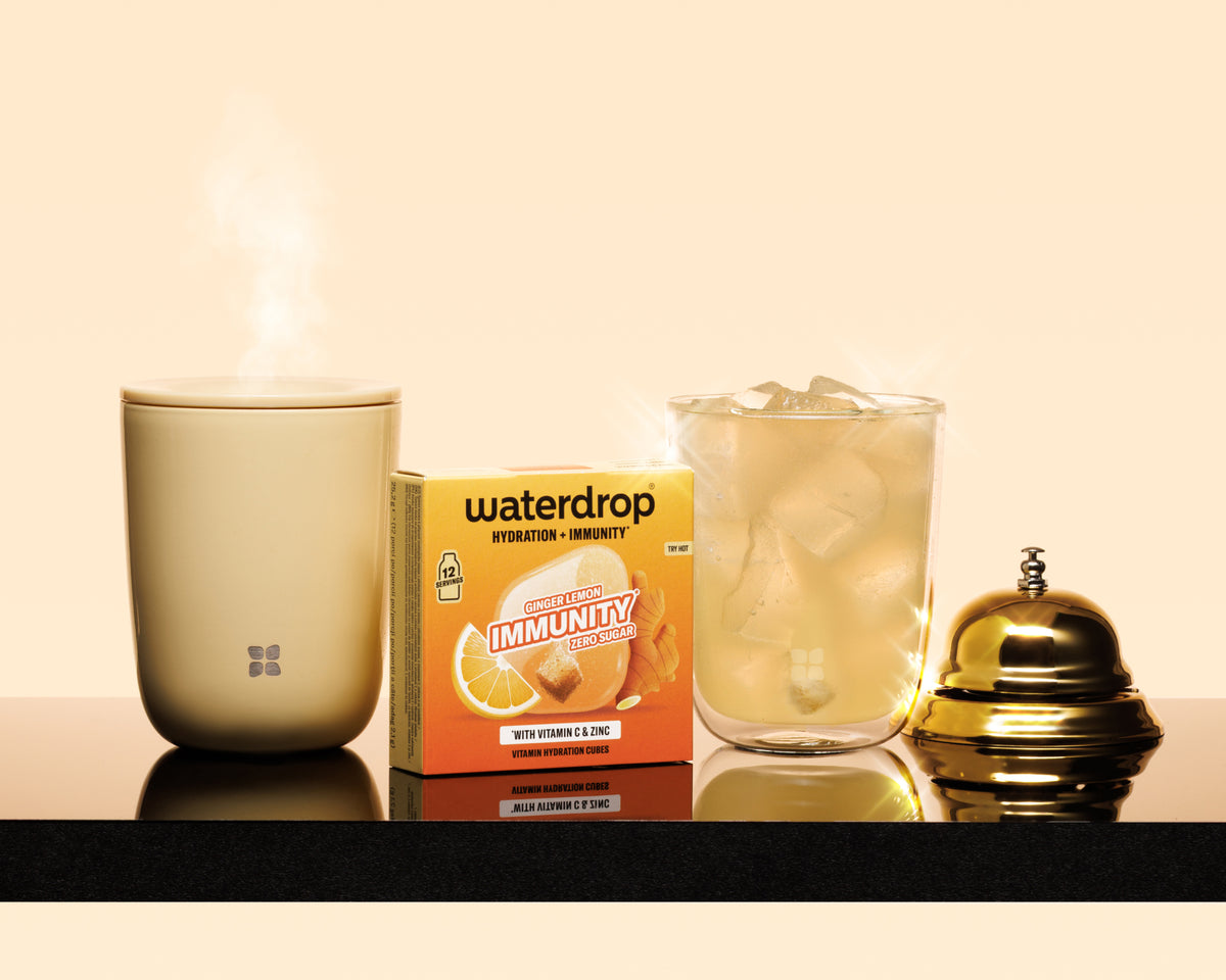 Stoomende beige mok, doos immuniteitsproduct, glas met ijs en een gouden bel op een zwarte aanrecht/schreef.