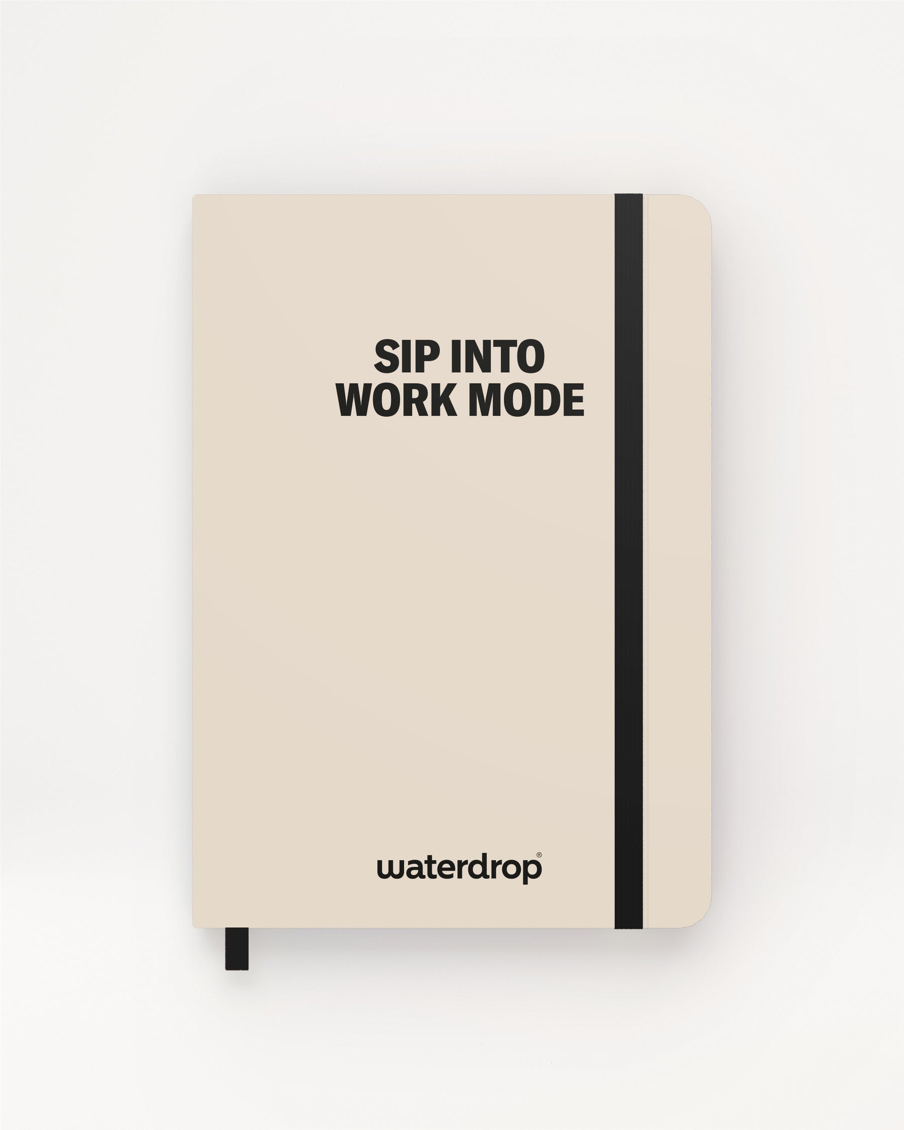 Beige hardcover notitieboek met zwarte elastiek en bladwijzer op een lichte achtergrond.