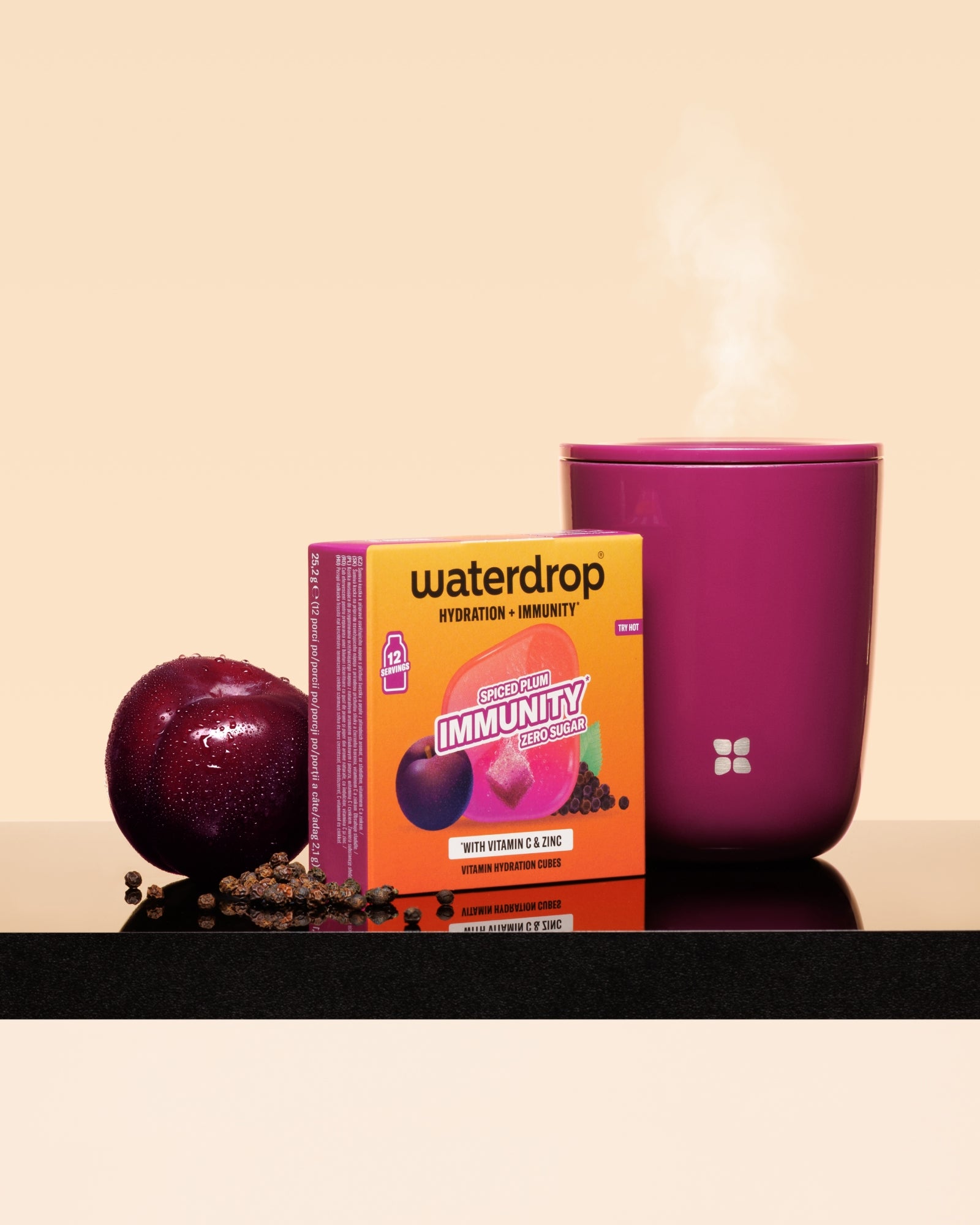 Waterdrop immuniteitsboost-doos naast een pruim en een dampende roze mok op een zwarte ondergrond.